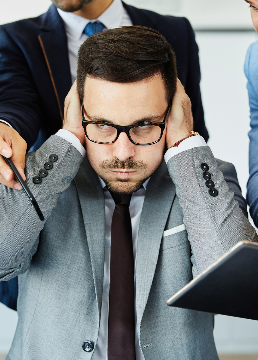 Stressed employee covering ears during workplace tension.